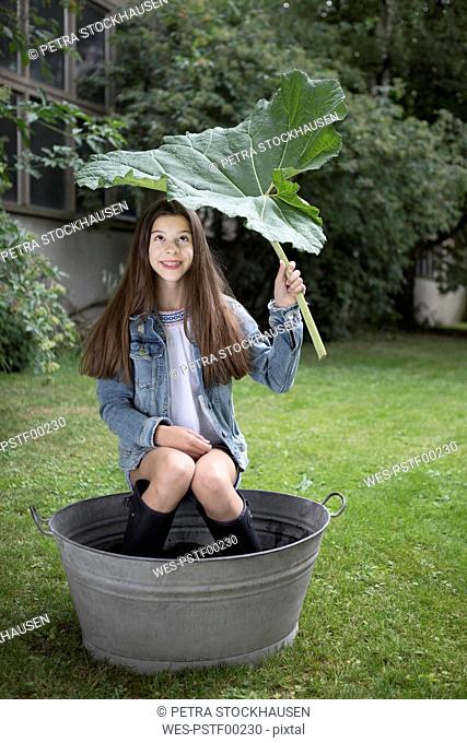 Portrait of smiling girl sitting under big in tub in in the garden