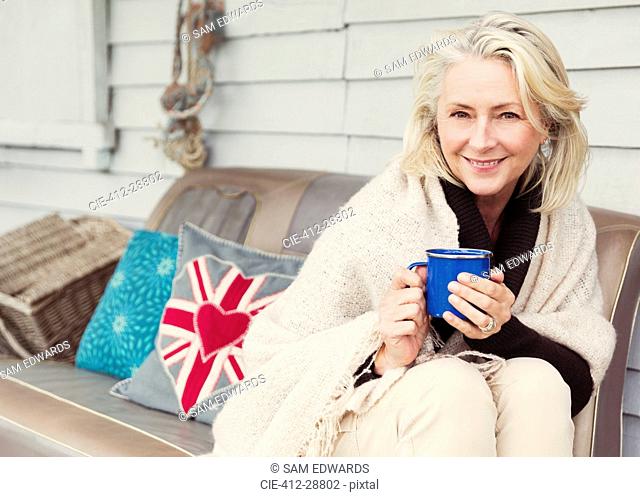 Portrait smiling senior woman drinking coffee on patio sofa