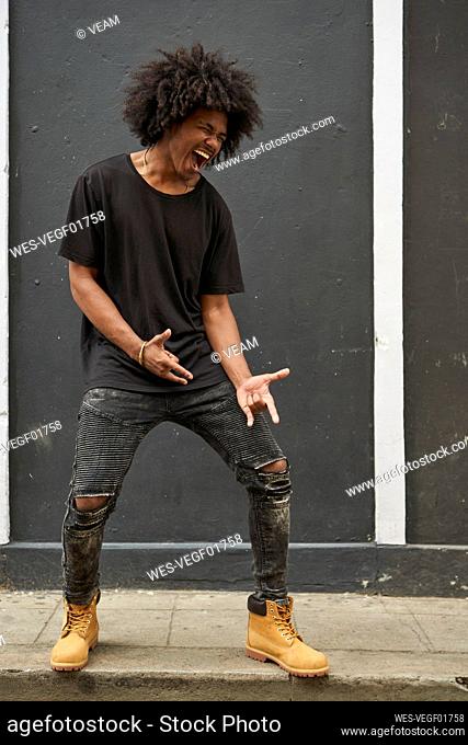 Young black man with afro singing and dancing in front of grey wall