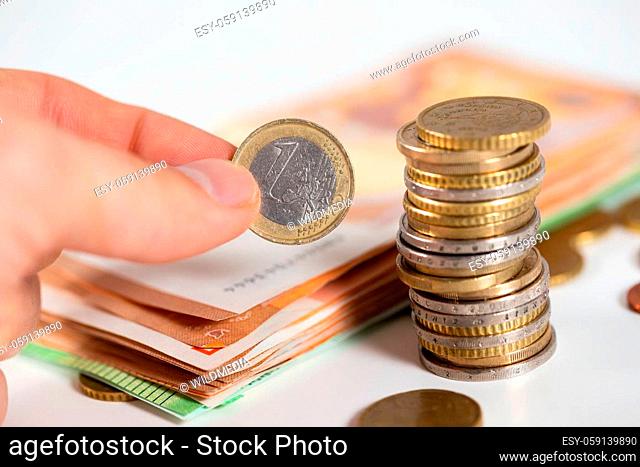 Human hand putting one euro to the stack on white table. Person holding coins in figers next to money stock. Finance managment during epidemic situation
