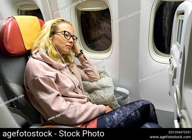 Tired blonde casual caucasian lady napping on uncomfortable seat while traveling by airplane. Commercial transportation by planes