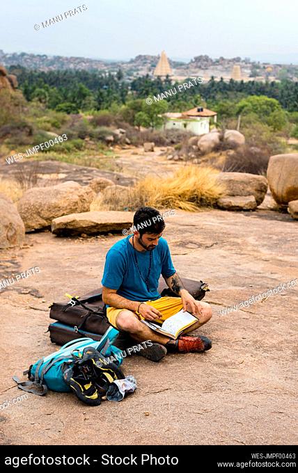 Young man reading book while sitting on land, Karnataka, Hampi, India