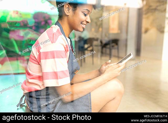 Smiling woman text messaging through smart phone seen through glass