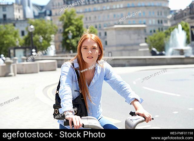 Beautiful woman riding hire bike on city street during sunny day
