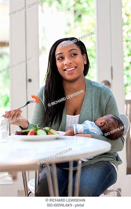 Mother holding baby son and having lunch