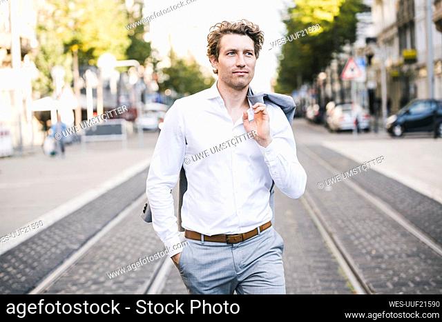 Smiling man walking with hand in pocket and jacket over shoulder in city