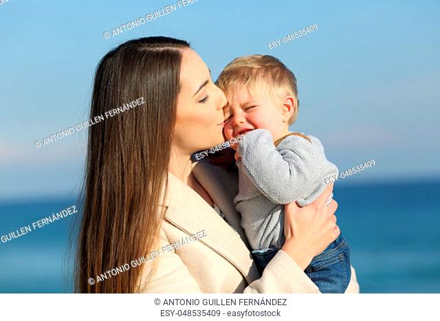Happy mother kissing her angry son outdoors on the beach