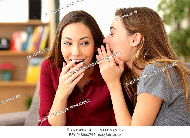 Portrait of a gossip girl telling a secret in the ear to her friend sitting on a couch at home