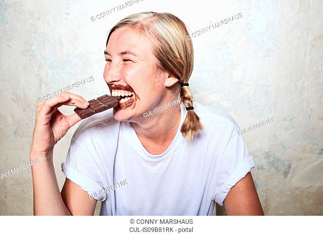 Woman eating bar of chocolate, chocolate around mouth, laughing