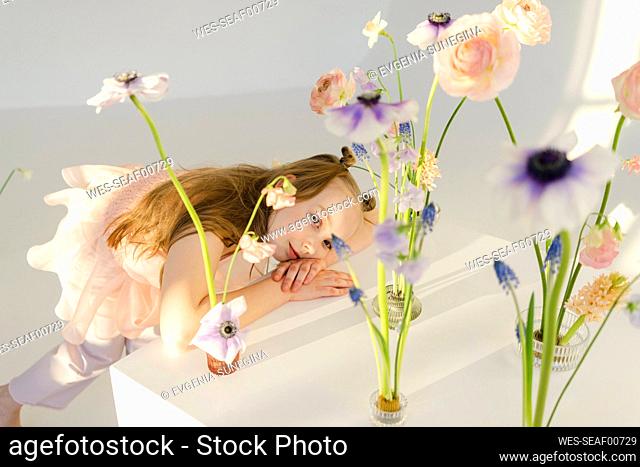Cute girl leaning on table by flowers in front of white wall