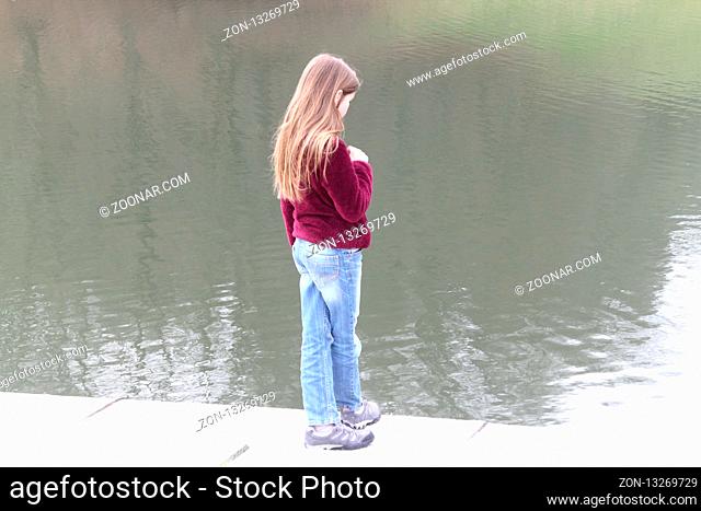 A blond girl stands on the shore of a lake