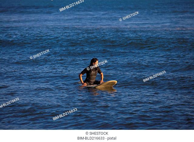 Hispanic surfer floating on surfboard in ocean