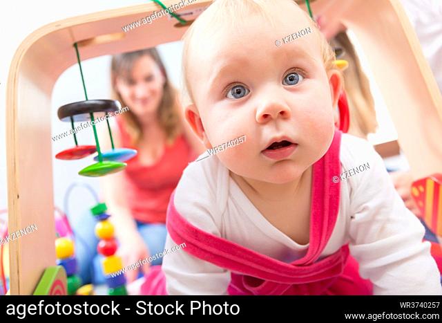 Close-up portrait of a cute baby girl with blue eyes and an intelligent facial expression, while playing on the floor with her mother at home