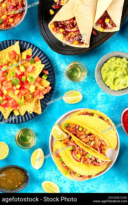 Mexican foodflatlay, overhead shot on a turquoise background. Nachos, tequila with limes, taco shells, burritos, guacamole