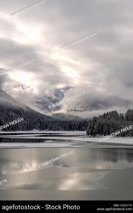 The Sylvensteinspeichersee at the edge of the Karwendel mountains in the Bavarian Alps in winter with snow and partly with ice, as well as cloud atmosphere