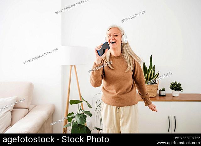 Happy woman wearing headphones dancing and singing at home