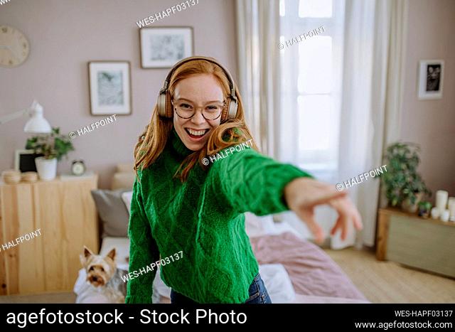 Happy woman dancing listening music through wireless headphones at home
