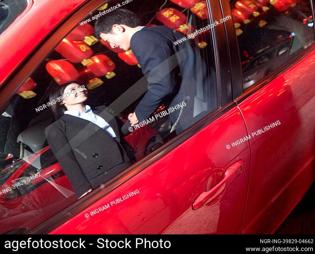 Coworkers handshaking next to the car at night, red lanterns on the background