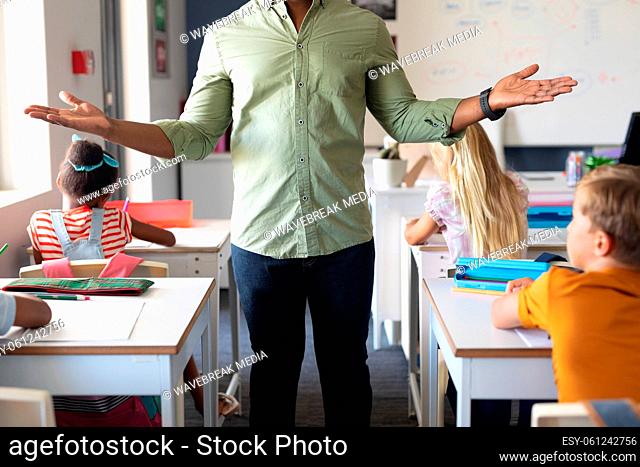 Midsection of african american young male teacher gesturing while standing by students in classroom