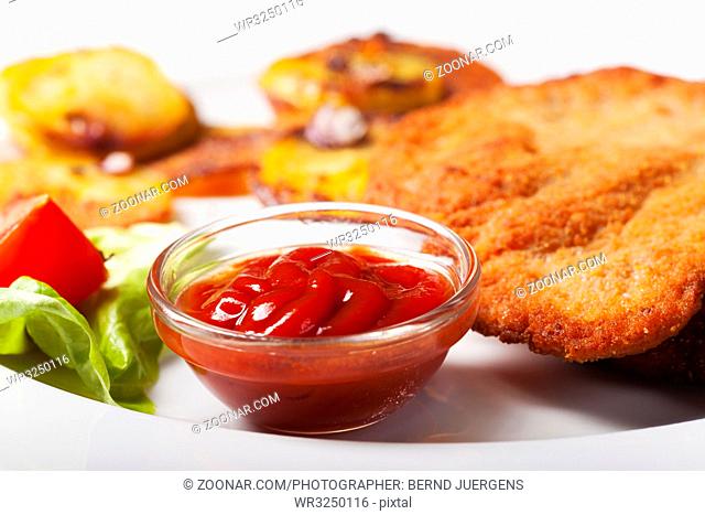 Ketchup mit einem Wiener Schnitzel und Bratkartoffeln