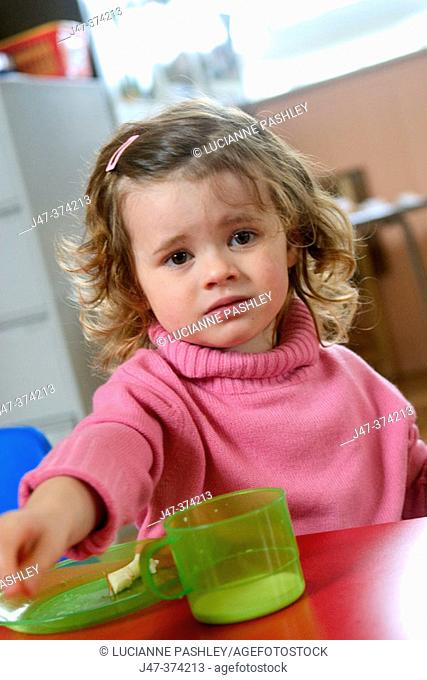 Three year old girl with a plate and cup, looking miserable