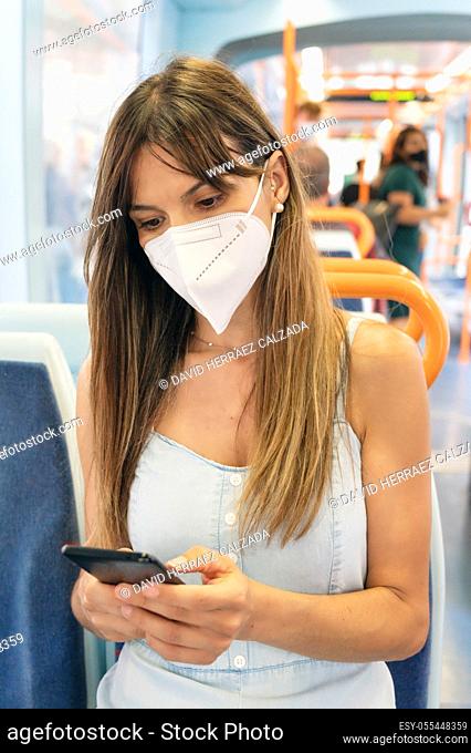 Woman wearing face mask using mobile phone onboard train. High quality photo