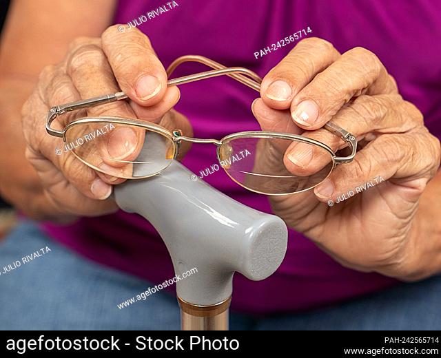 Old wrinkled woman hands holding glasses on a walking stick || Model approval available