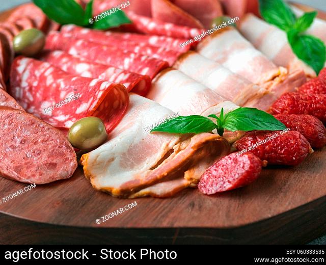 Antipasto set platter on wooden plate close up. Cold smoked meat plate with sausage, sliced ham, prosciutto, bacon, olives and basil