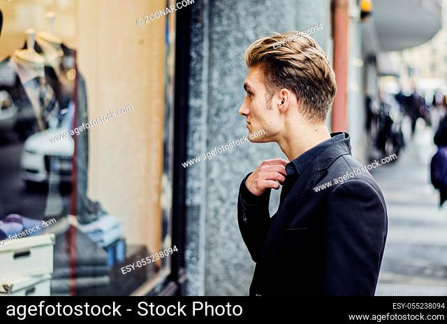 Handsome Young Man in Black Elegant Suit Looking at Displayed Fashion Items in Glass Window Boutique at the Street Side