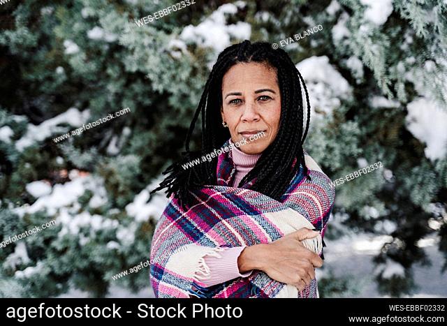 Mature woman with arms crossed wrapped in plaid shawl at park