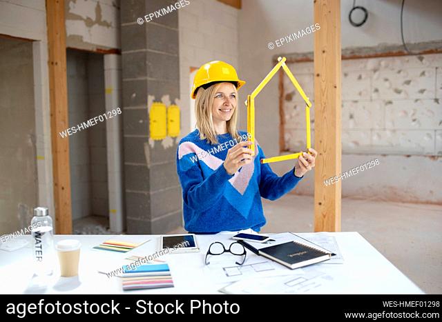 Smiling female building contractor making house shape with folding ruler at construction site