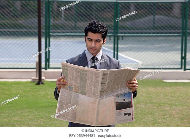 Young male executive reading newspaper in a tennis court