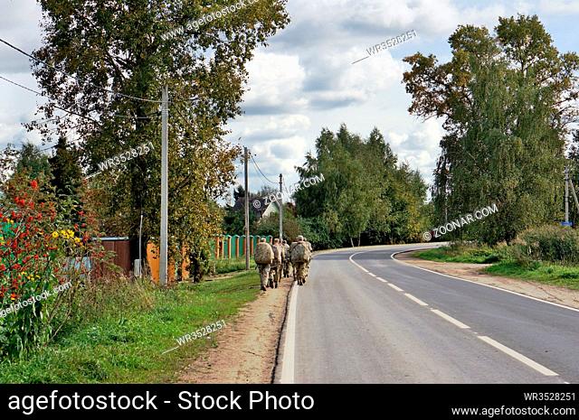 Russian soldiers of special forces leave the village road for field exercises. View from the back. No recognizable person or logo