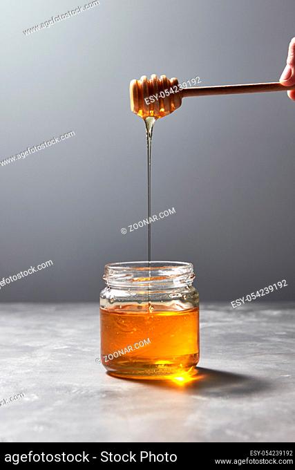 Wooden stick with natural flower honey in a womans hand above a gray concrete table, place for text. Traditional useful natural sweetness
