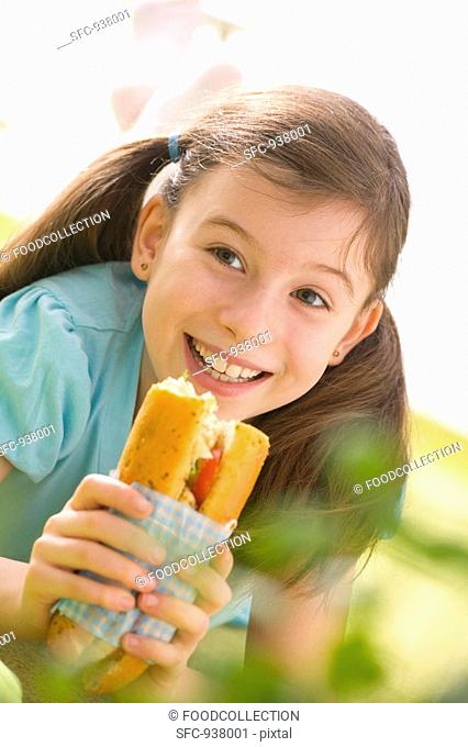Girl eating fish and salad sandwich at picnic