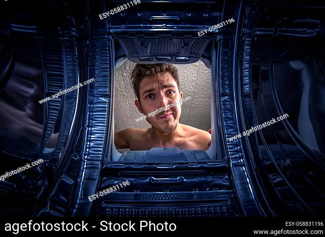 Young man doing laundry View from the inside of broken top loaded washing machine
