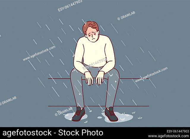 Unhappy man sitting on bench under rain feeling depressed and lonely. Sad male suffer from depression or mental problems. Stress and solitude