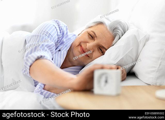 happy senior woman with alarm clock in bed at home