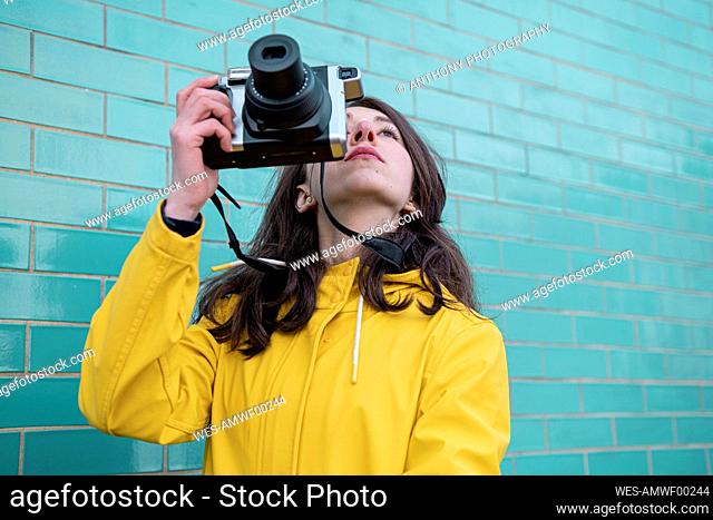 Young woman with camera standing by brick wall