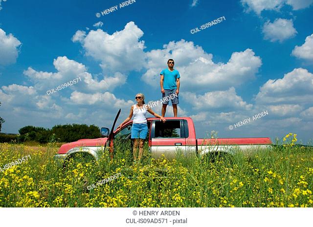 Mother and son with pickup truck in field, son standing on top of truck