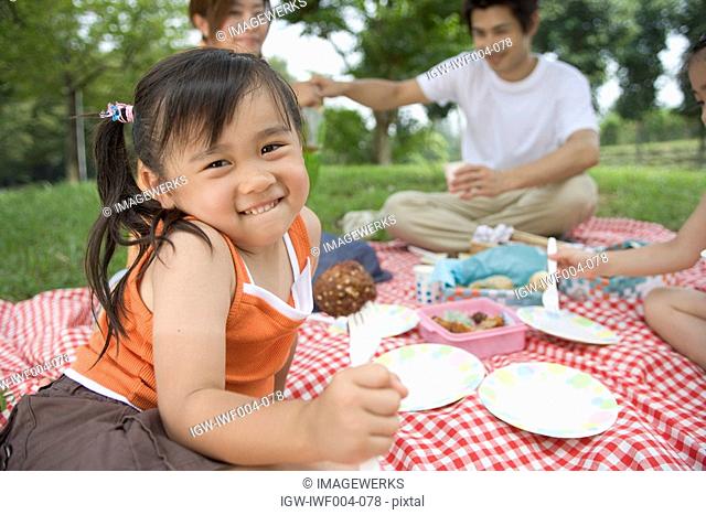 A girl having lunch by the trees with her family