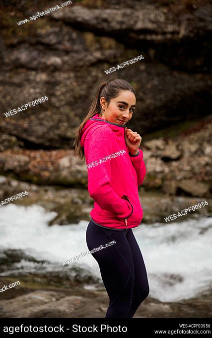 Sportswoman wearing tracksuit smiling while standing by river at Ordesa National Park, Huesca, Spain