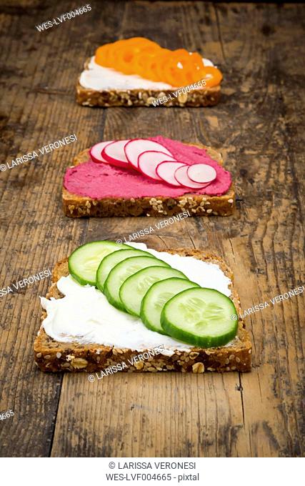 Three wholemeal bread slices with different spreads and toppings on wood