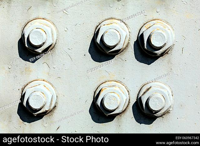 Six large nuts and bolts on gray steel plate of rail bridge, lit by bright sun. Abstract industrial background
