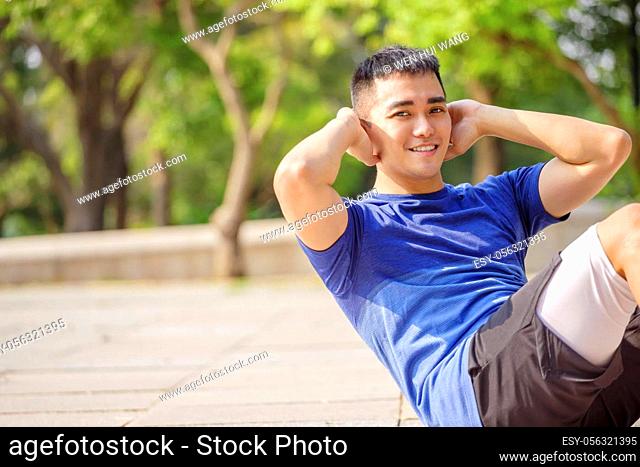young man training and doing sit ups in park