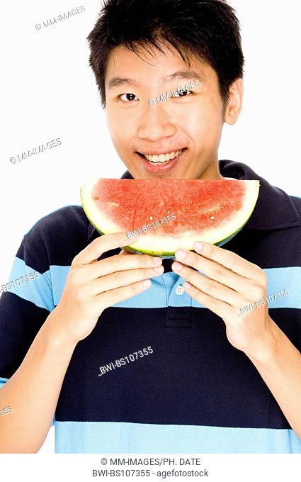 A young Chinese man eating a slice of melon