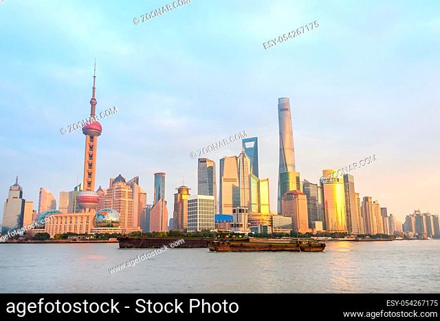 Shanghai skyline with modern architecture at sunset, rusty barges by city embankment, China