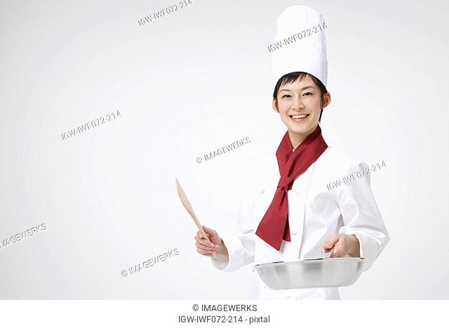 Female chef holding wooden spoon and pan, smiling, portrait