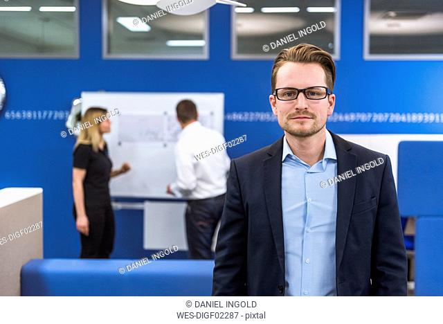 Businessman standing in conference room, while colleagues working with flipchart in background