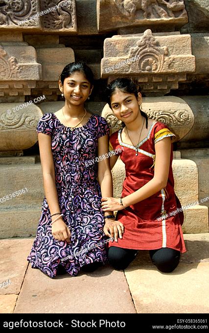 Two smiling sisters sitting at the backdrop of temple at Pattadakal in Bagalkot district, Karnataka, India, Asia
